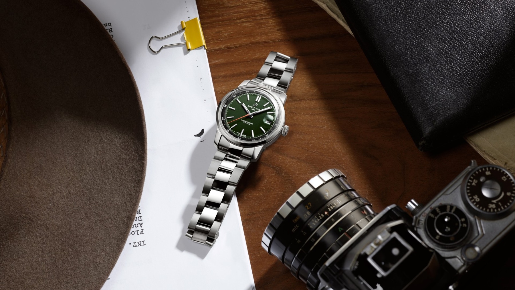 Green Breitling Top Time B31 on a steel bracelet beside a camera and papers